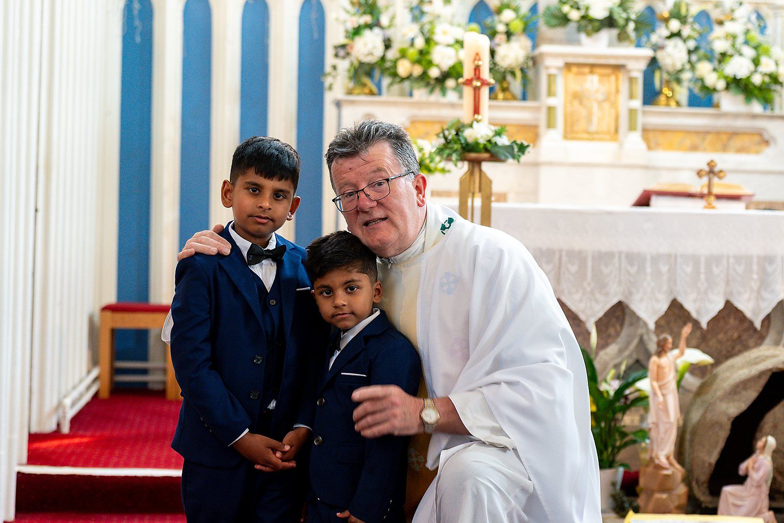 Two boys in navy suits with the priest at the altar on their First Holy Communion