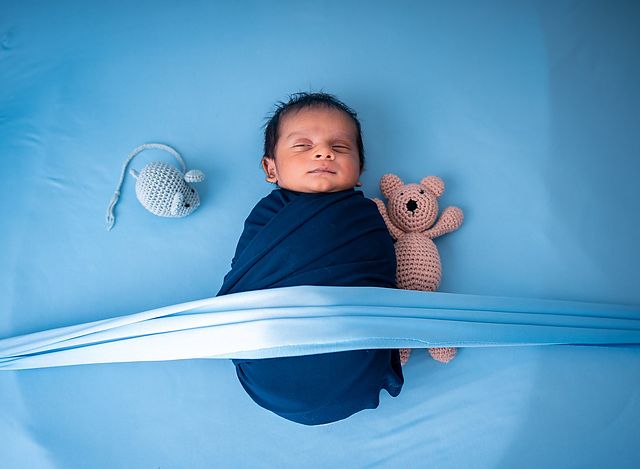 Newborn in a blue wrap with a teddy