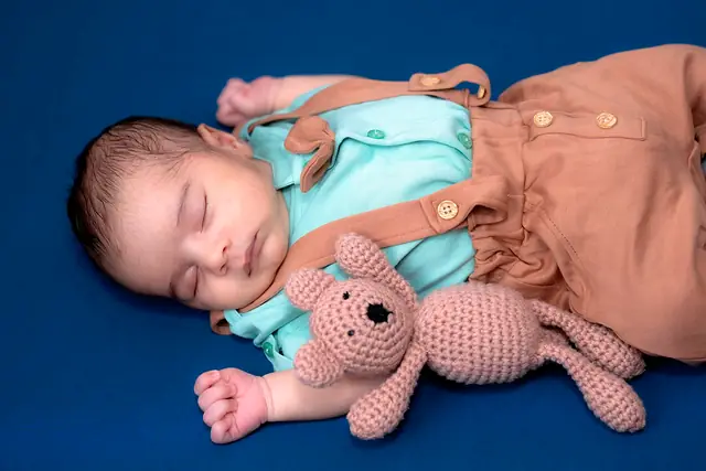 Newborn with knitted teddy on navy backdrop