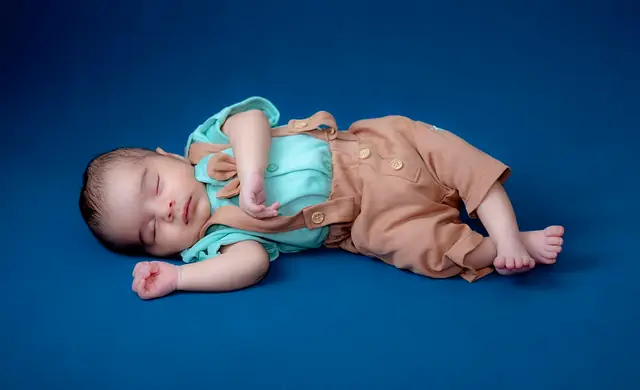 Newborn in brown dungarees on blue backdrop