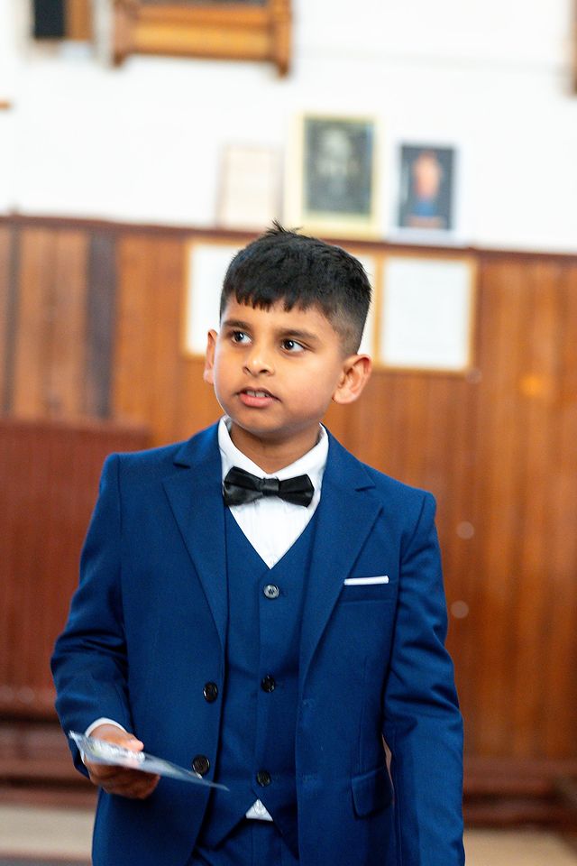 Boy in a navy suit holding a card, indoors